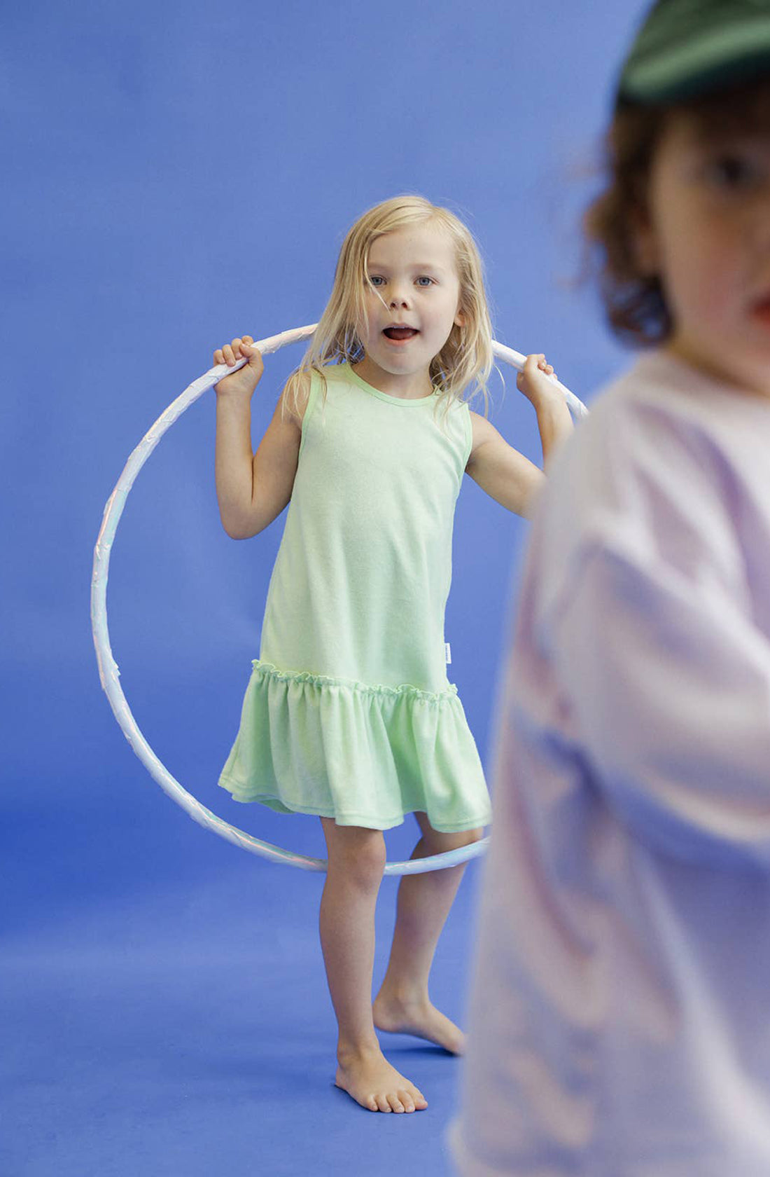 A young girl wearing the spin me round terry towelling dress in green holding a hula hoop.