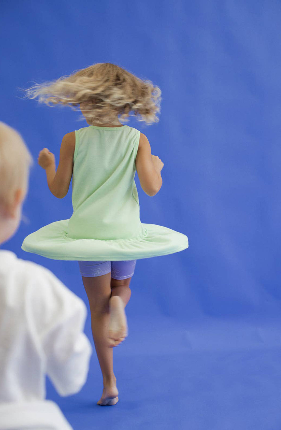 A young girl wearing the spin me round terry towelling dress in green spinning on her tippy toes.