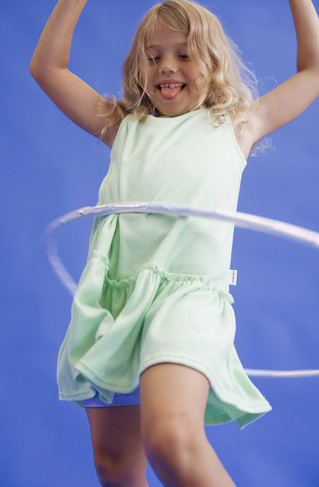 A young girl wearing the spin me round terry towelling dress in green spinning a hula hoop around her waist.