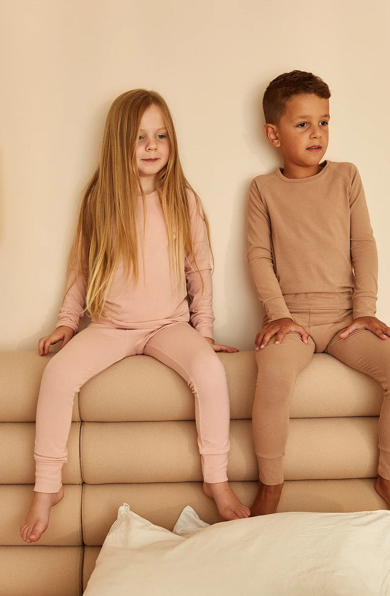 Boy and girl sitting on back of a couch wearing the sleep sets in misty rose and tawny brown