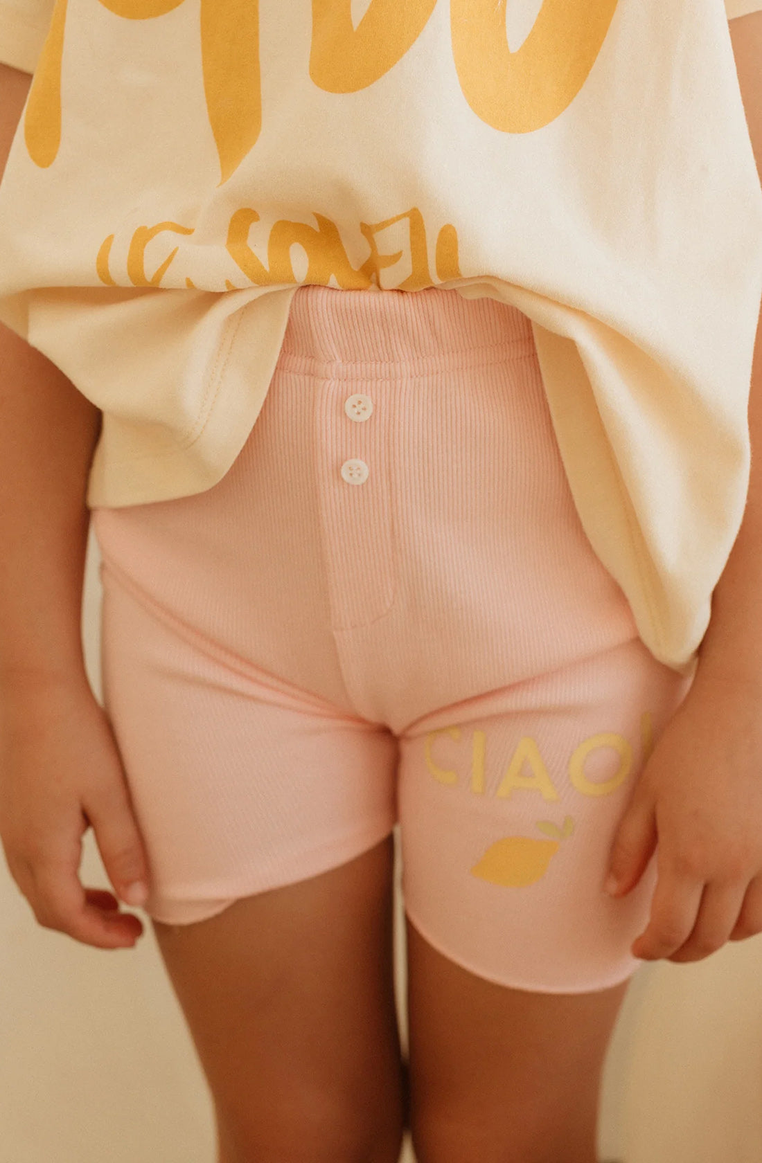 Close up of pink ribbed bike shorts with buttons at the centre front and ciao print on the right thigh