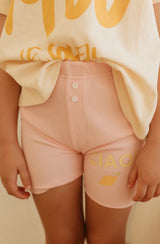 Close up of pink ribbed bike shorts with buttons at the centre front and ciao print on the right thigh