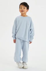 Boy wearing a matching pale blue fleece set standing against a white background