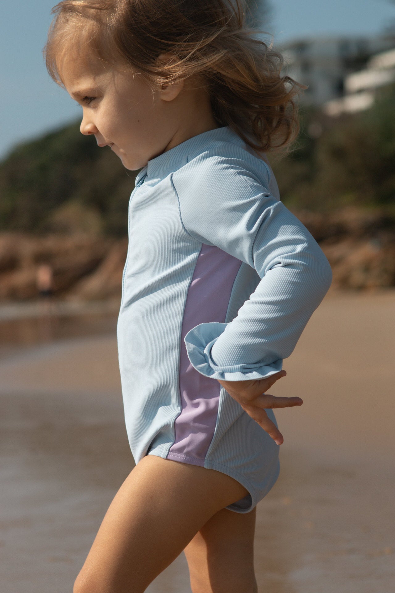 Child wearing a light blue and purple swimsuit on a beach