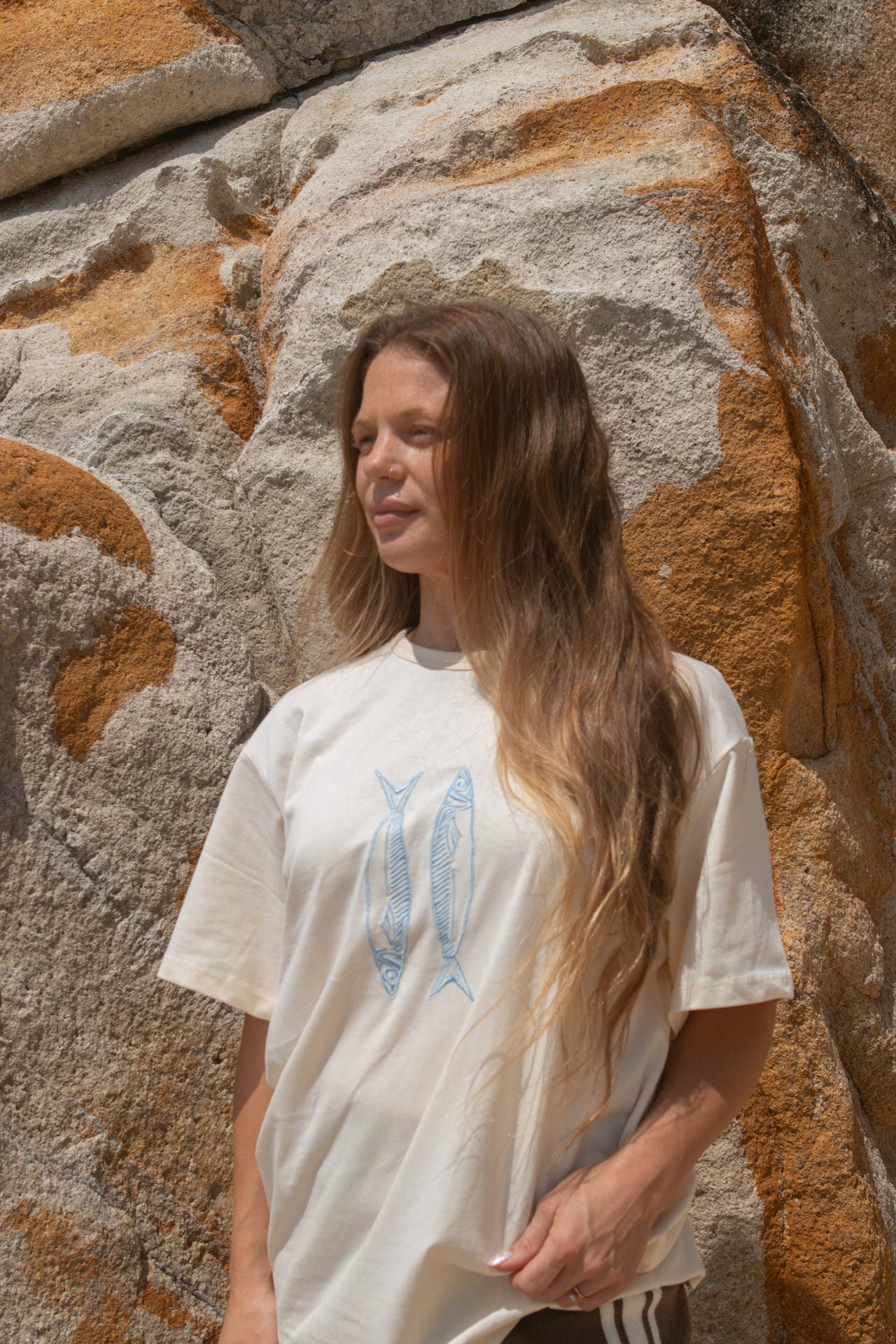 Woman wearing a white t-shirt with a blue fish against a stone wall.