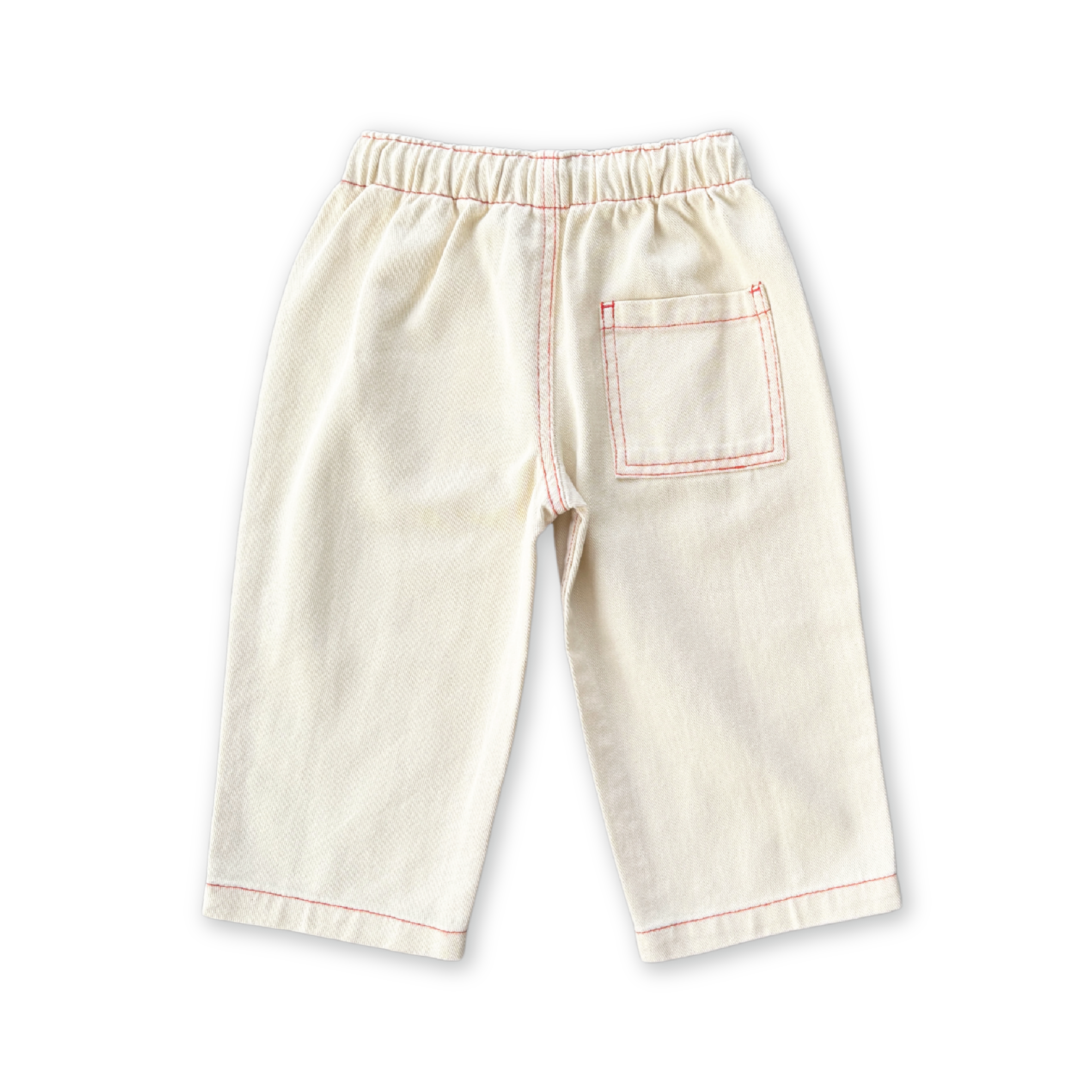 The GROWN Organic Everyday Denim Pant Milk is a pair of cream-colored kids’ pants made from organic cotton, featuring red stitching, a relaxed fit, elastic waistband, and back pocket—shown on a black background.