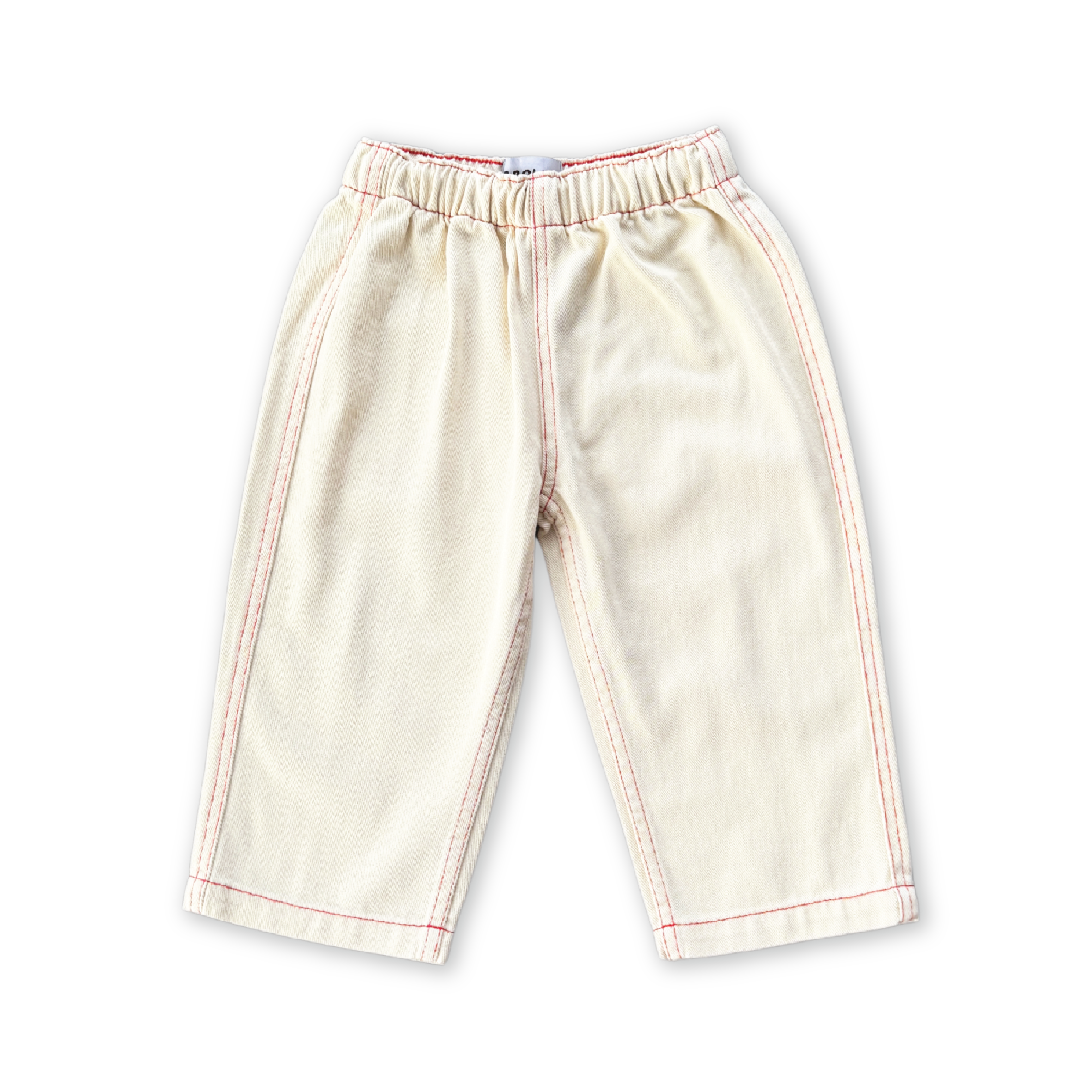 The GROWN Organic Everyday Denim Pant Milk is a pair of light beige children's pants made from organic cotton, featuring an elastic waistband and red seam stitching, shown on a black background.