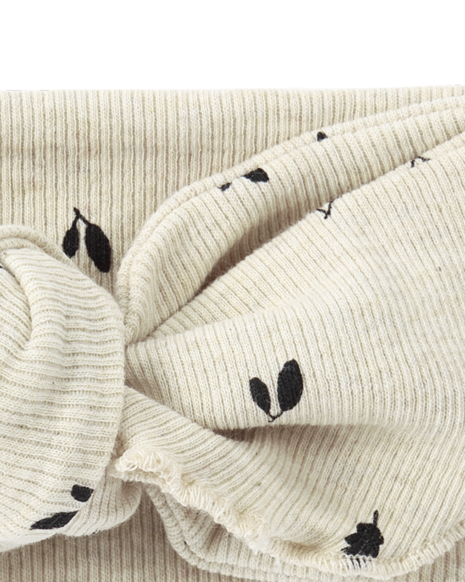 A close-up image of the Elastic Headband Fall Leaves by SUSUKOSHI, showcasing its cream-colored ribbed fabric adorned with black leaf patterns. Made from organic cotton, this headband features a twisted knot design at the front. The texture and details of the knit fabric are clearly visible.