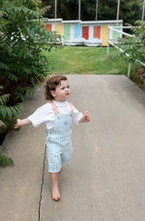 Toddler walking towards the camera wearing the Hola Ninch Overalls with white tee