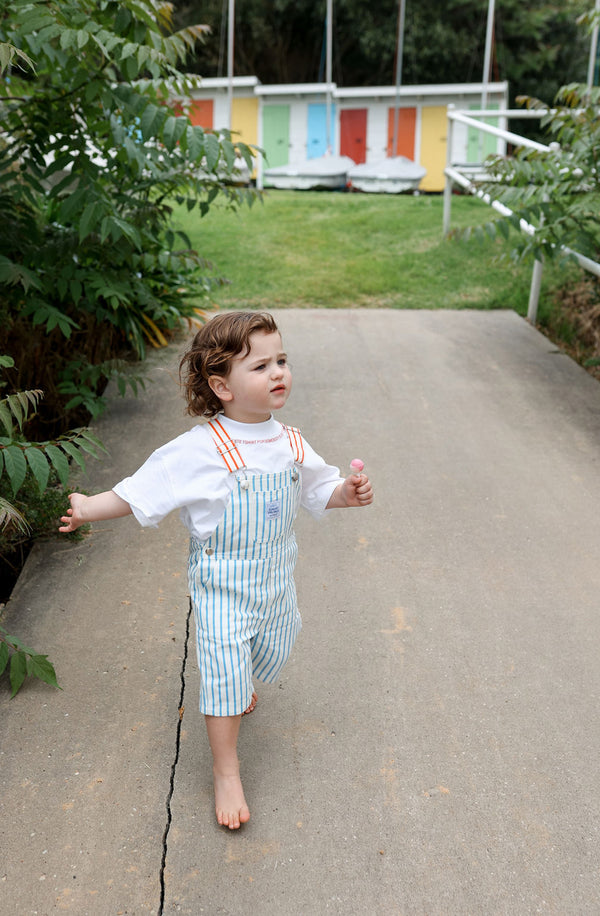 Toddler walking towards the camera wearing the Hola Ninch Overalls with white tee