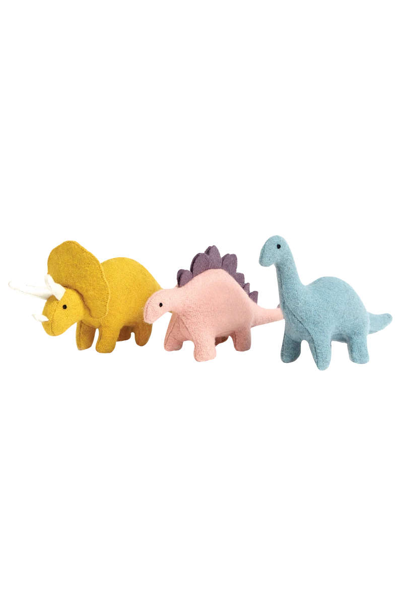 Three prehistoric pals from the Holdie Dinosaurs collection by Olli Ella are lined up side by side. From left to right, there is a yellow triceratops, a pink stegosaurus with purple plates on its back, and a blue brontosaurus. Each of these Holdie Folk Dinosaurs boasts a simple, cute design made from handmade soft wool blend fabric.