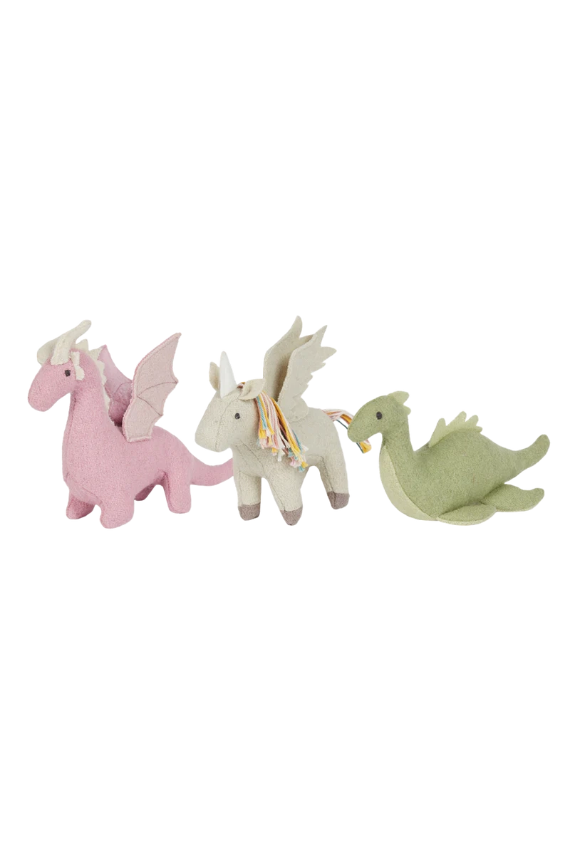 Three fabric children's toys made from a soft wool blend: an OLLI ELLA Holdie Magical Creatures pink dragon with wings and horns, a white unicorn with colorful hair and silver horn, and a green dragon with wings and horns, lined up in a row from left to right.