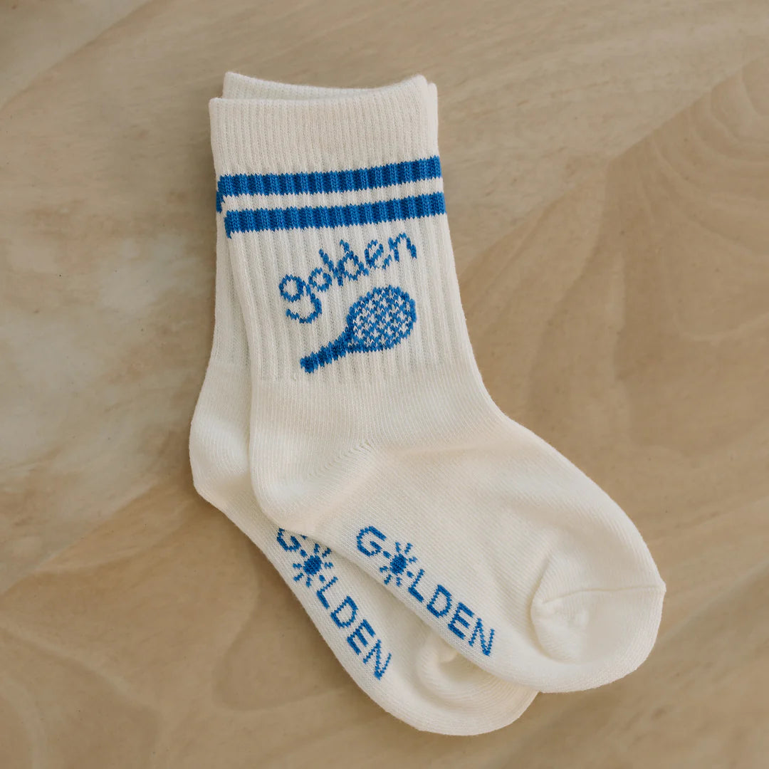 Vanilla Retro Boy socks by GOLDEN CHILDREN, featuring two blue stripes around the cuff. The outer side is adorned with a tennis racket design and "golden" printed in blue, while "GOLDEN" in block letters is displayed near the sole. These ribbed socks gracefully rest on a beige surface, evoking a Palm Beach lifestyle.