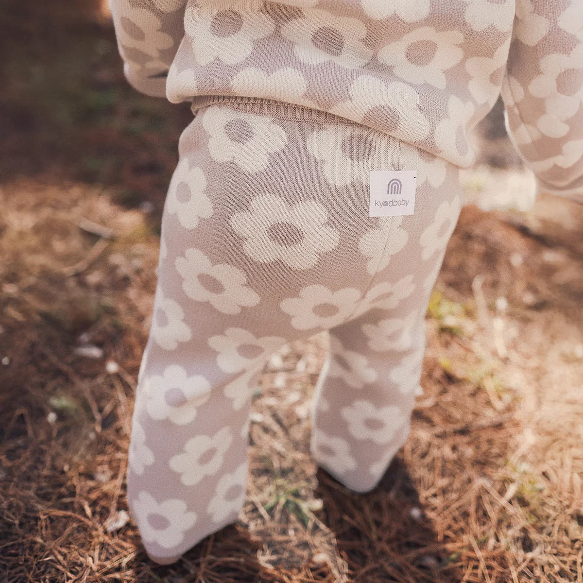 A baby in KYND BABY’s Kynd Baby - Knit Flare Pants Neutral Flower, crafted from organic cotton for a cozy, vintage-inspired look.