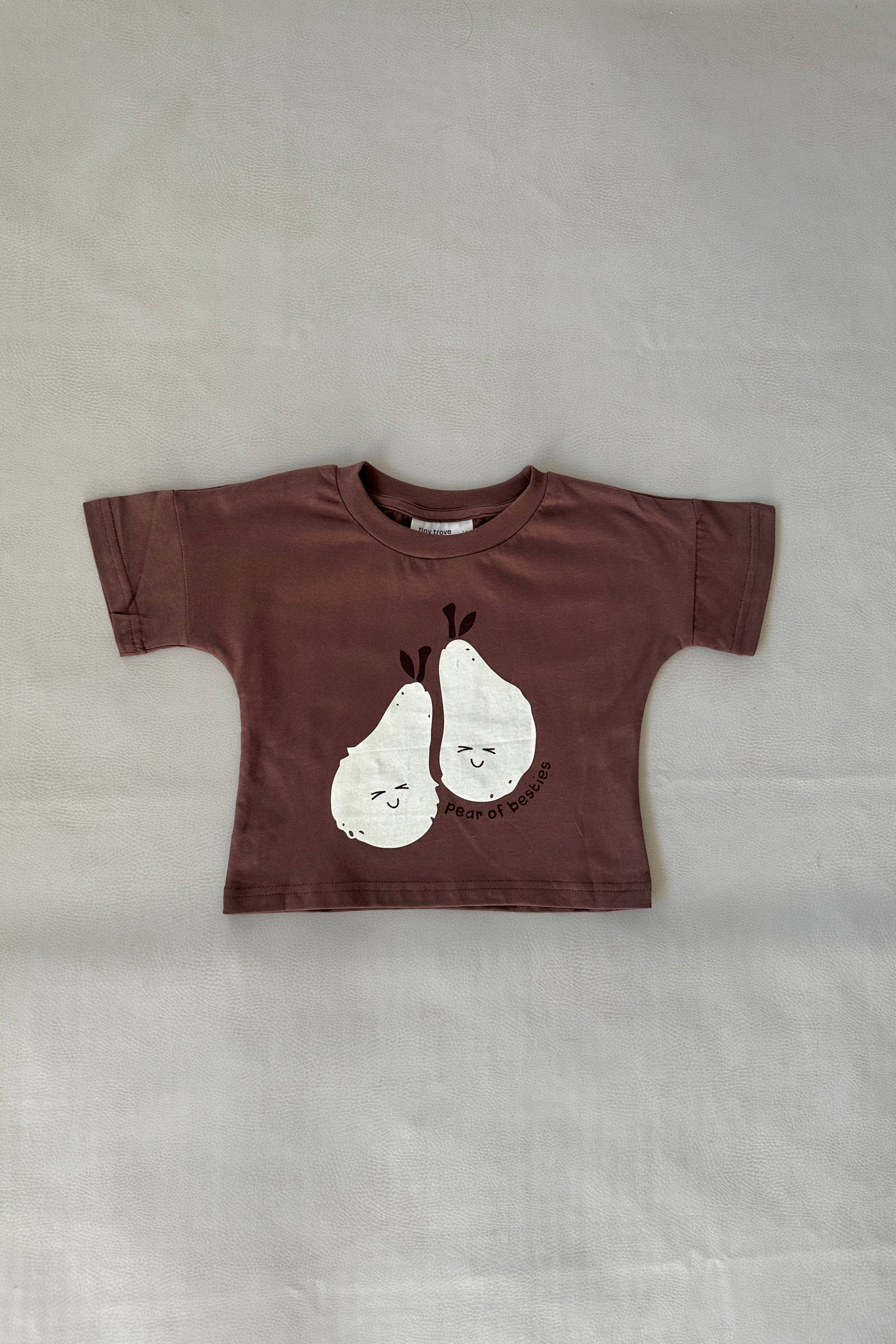 The Pear Relaxed Tee - Iced Chocolate from TINY TROVE is a small t-shirt in a relaxed fit, showcasing playful illustrations of two smiling pears with the charming text "pear of bears" beneath them. Made from 100% cotton, it ensures ultimate comfort.