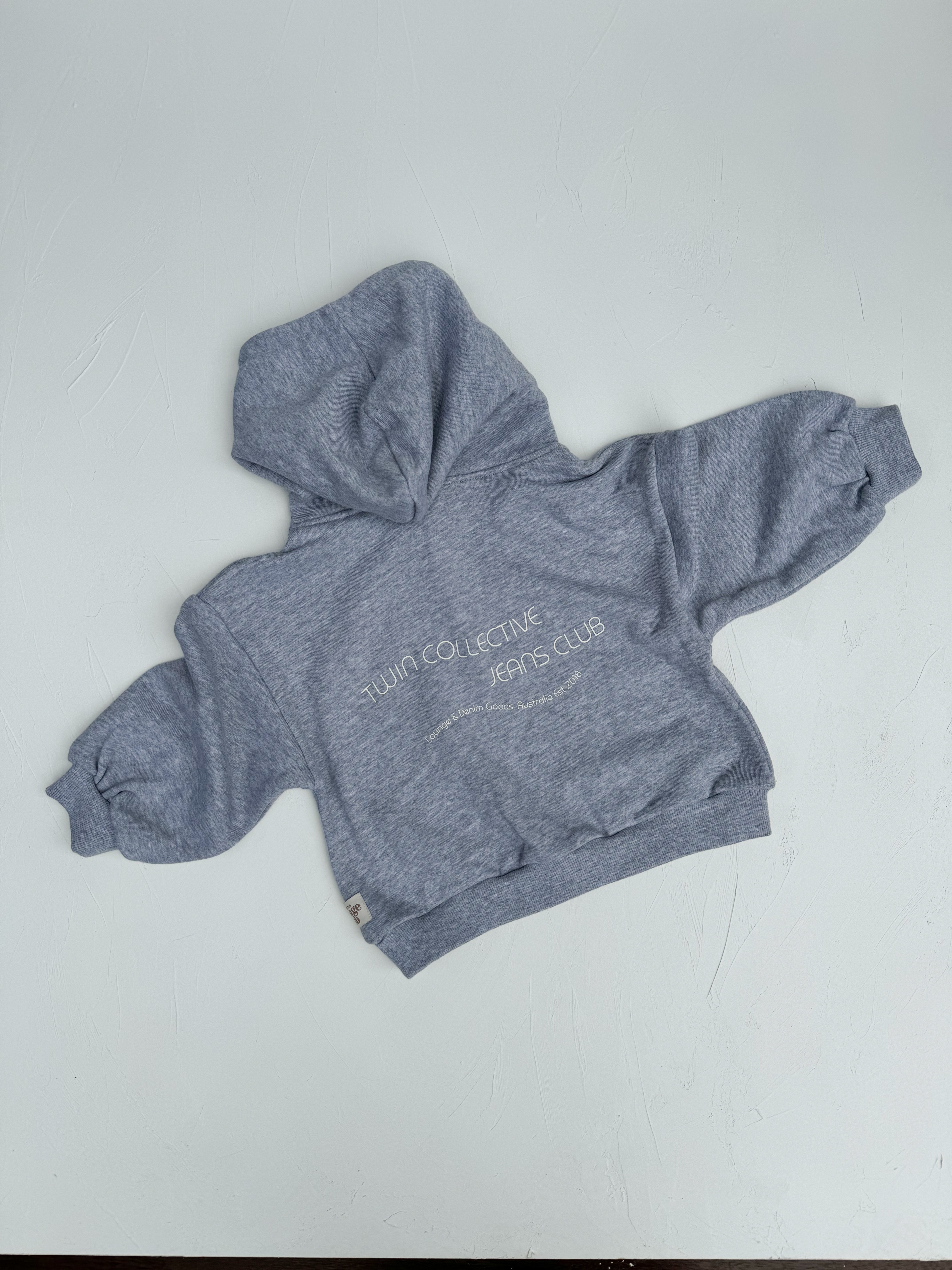 A toddler-sized TWIN COLLECTIVE Logo Hoodie Set in Grey Marle, with "TWIN COLLECTIVE JEANS CLUB" emblazoned on the front. This cozy Loopback Terry fleece hoodie features a front pocket and long sleeves, displayed laid flat on a white background.