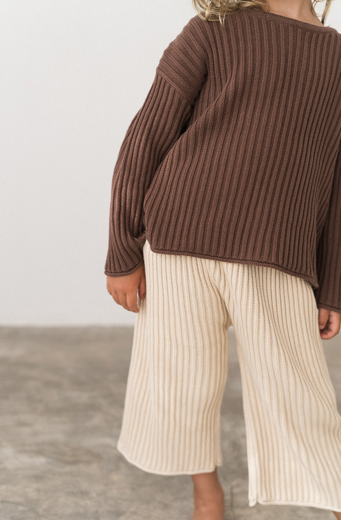 A young kid wearing the essential knit pants in biscuit and cocoa jumper.