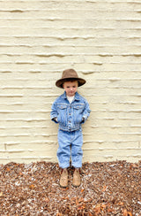 Boy standing against brick wall wearing denim jeans and denim jacket