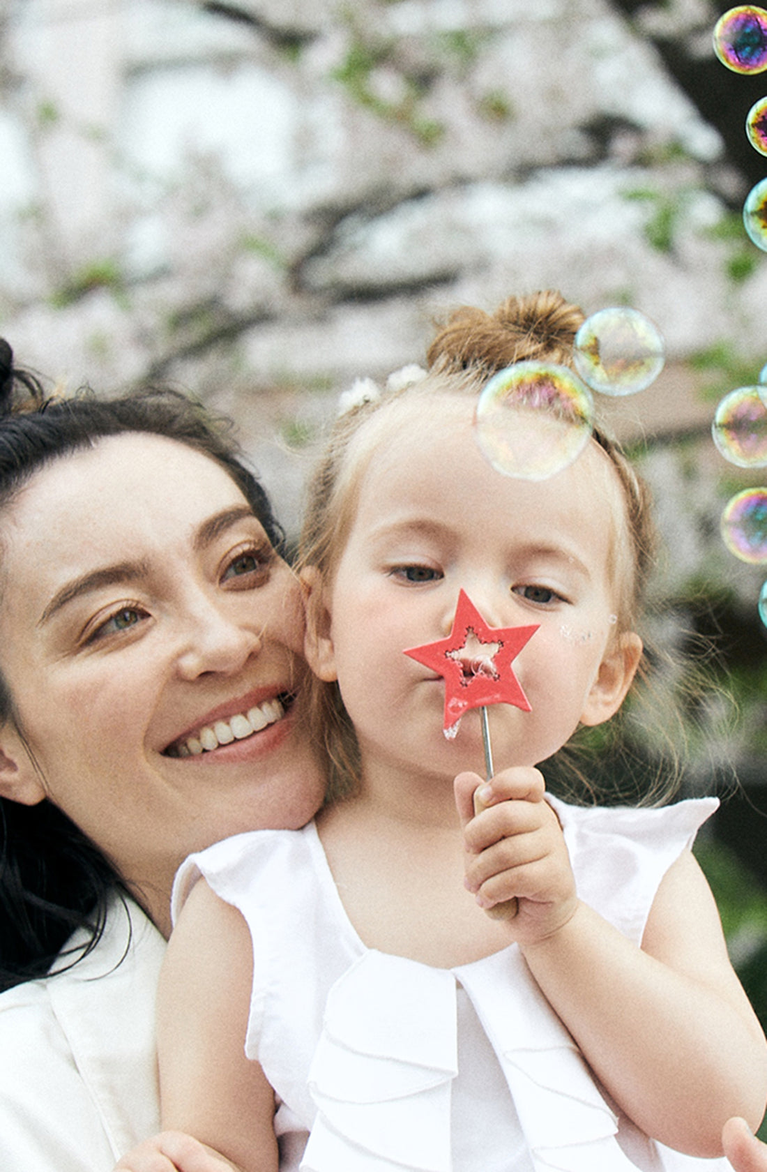 A young girl carried by her mother using the amechan reusable bubble wand set.