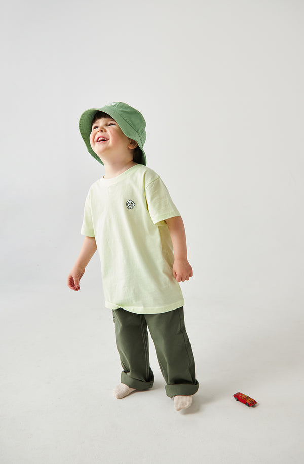 Boy wearing oversized Cruisin tee with green bucket hat and utility pants