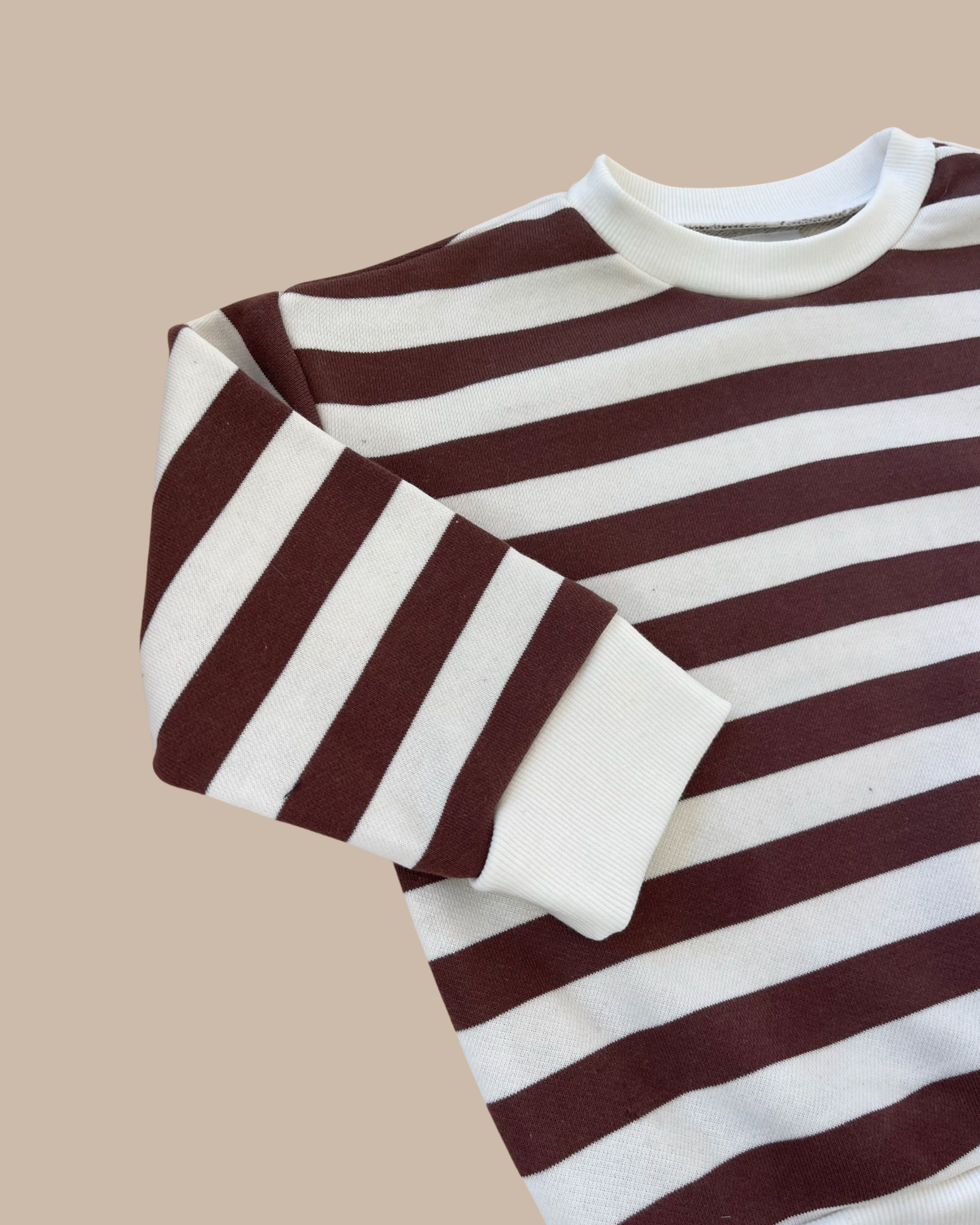 The Camden chocolate brown striped pullover on a light brown background with its arm folded over.