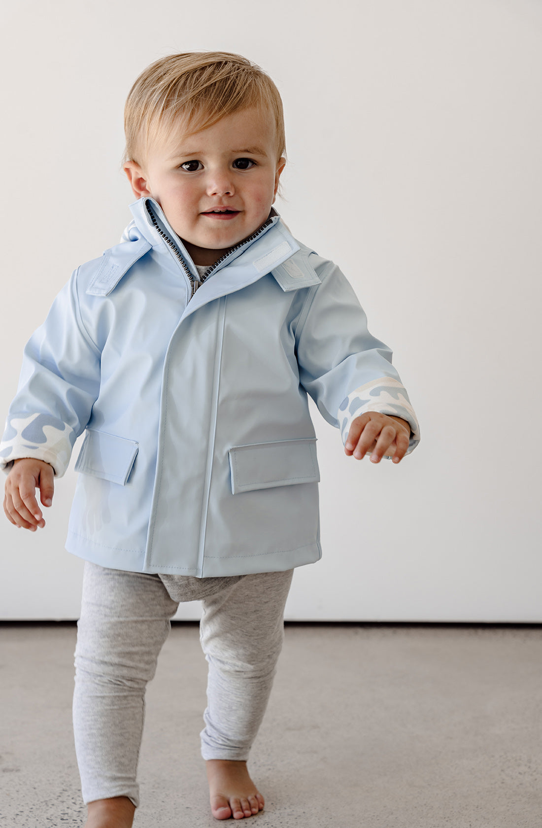 A toddler wearing the Kids rain jacket in bubblegum with grey pants.