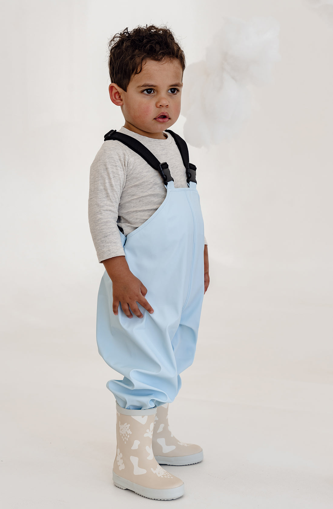 A toddler wearing the kids rain overalls with a long sleeve and gumboots.