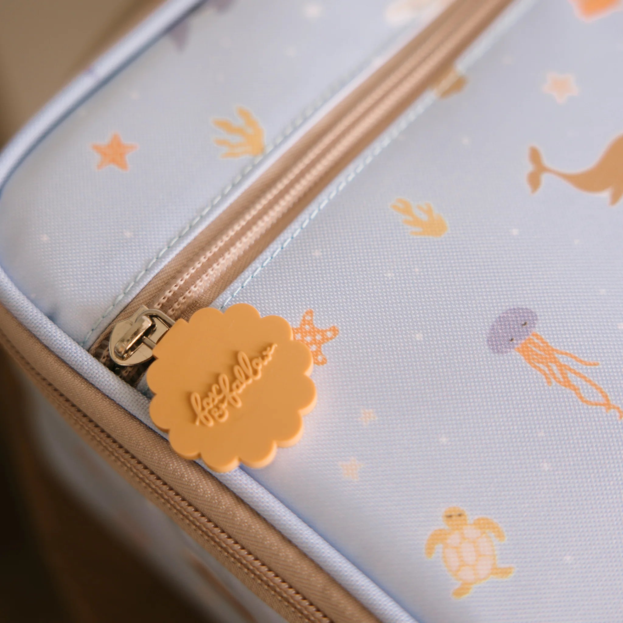 The Ocean Creatures Sky Lunch Bag by FOX & FALLOW is a pastel-colored travel bag made from waterproof fabric. It features a whimsical sea-themed pattern with jellyfish, turtles, starfish, and whales on a light blue background. A close-up view of its zipper showcases a cloud-shaped tag that says "Heys Yellow.