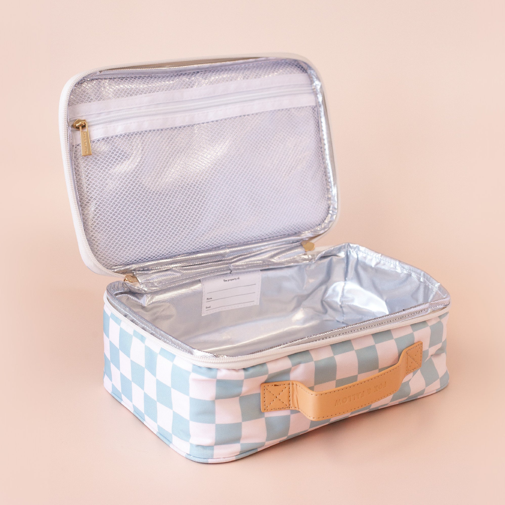 The FOX & FALLOW Sage Check Large Lunch Bag features a blue and white checkered pattern with a tan handle, silver insulated interior, mesh zippered pocket in the lid, and name label. Shown open on a light beige background.