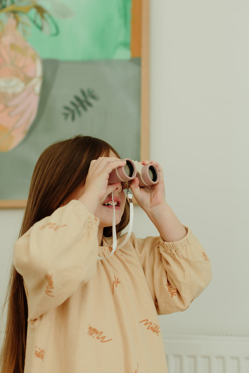 Girl holding binoculars to her eyes as if she is looking at something