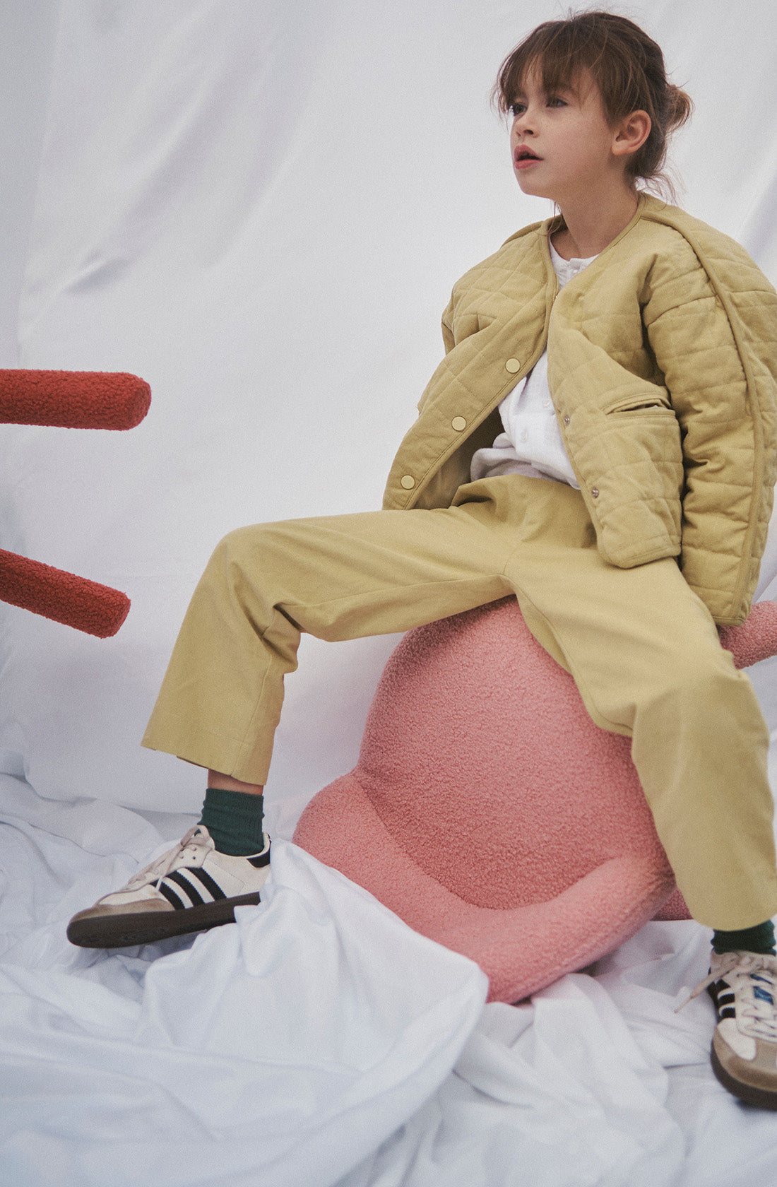 Young kid wearing the parker quilted jacket and mustard pants sitting on a chair.