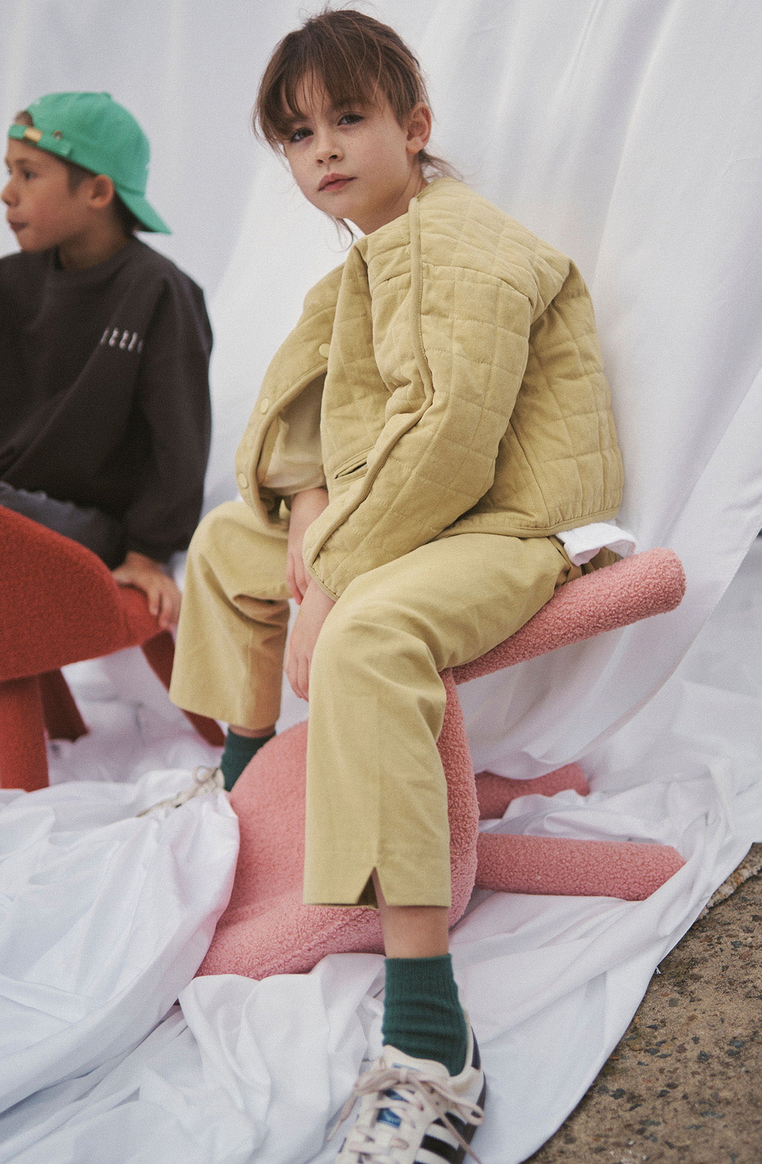 Young kid wearing the parker quilted jacket and mustard pants sitting on a chair.