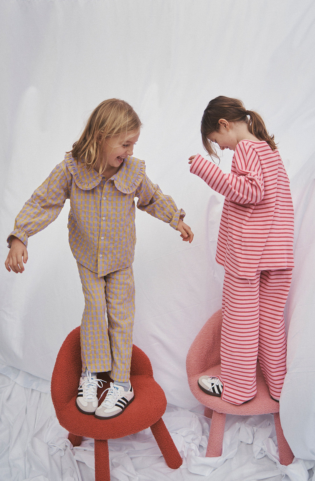 Two girls standing on chairs wearing matching sets in stripes and gingham styles.