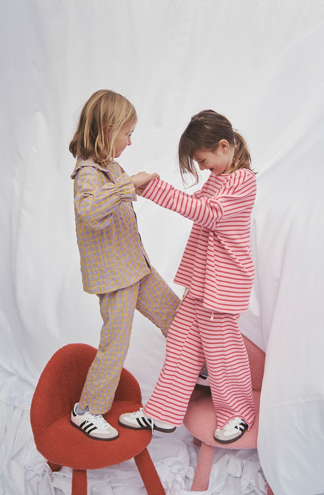 Two girls standing on chairs wearing matching sets in stripes and gingham style.