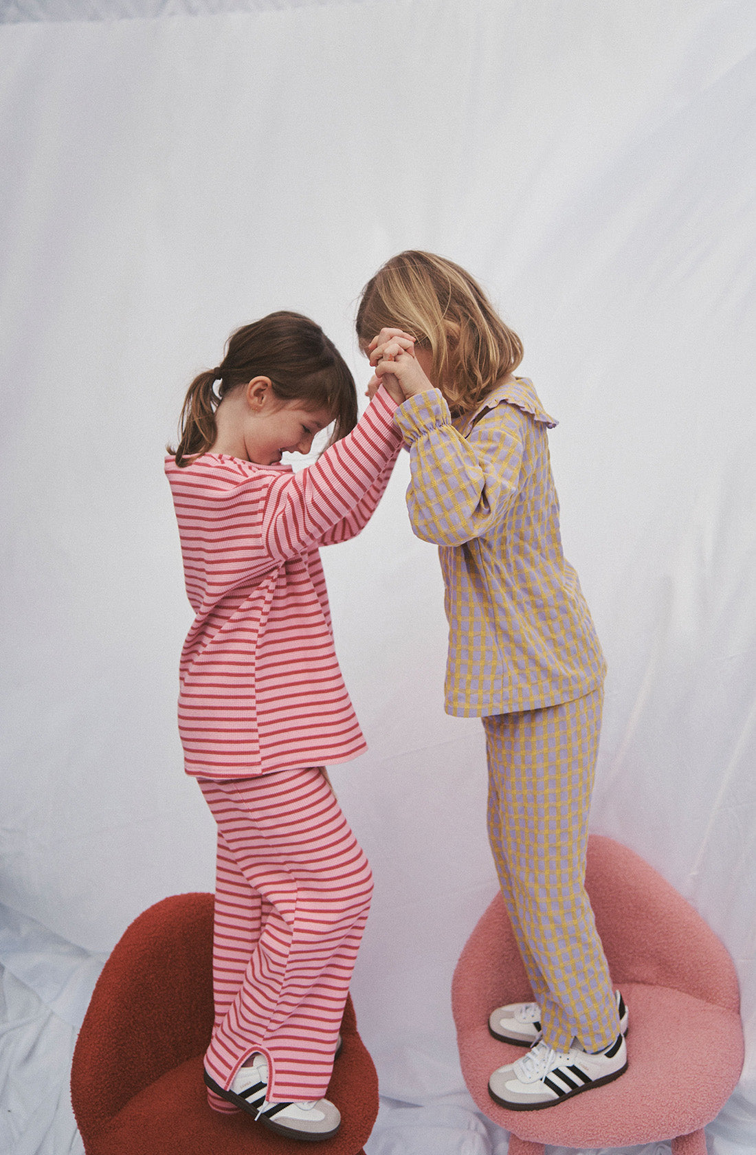 Young kid wearing the lucky lounge pant and matching top in candy apple holding hands with another girl while standing on chairs.