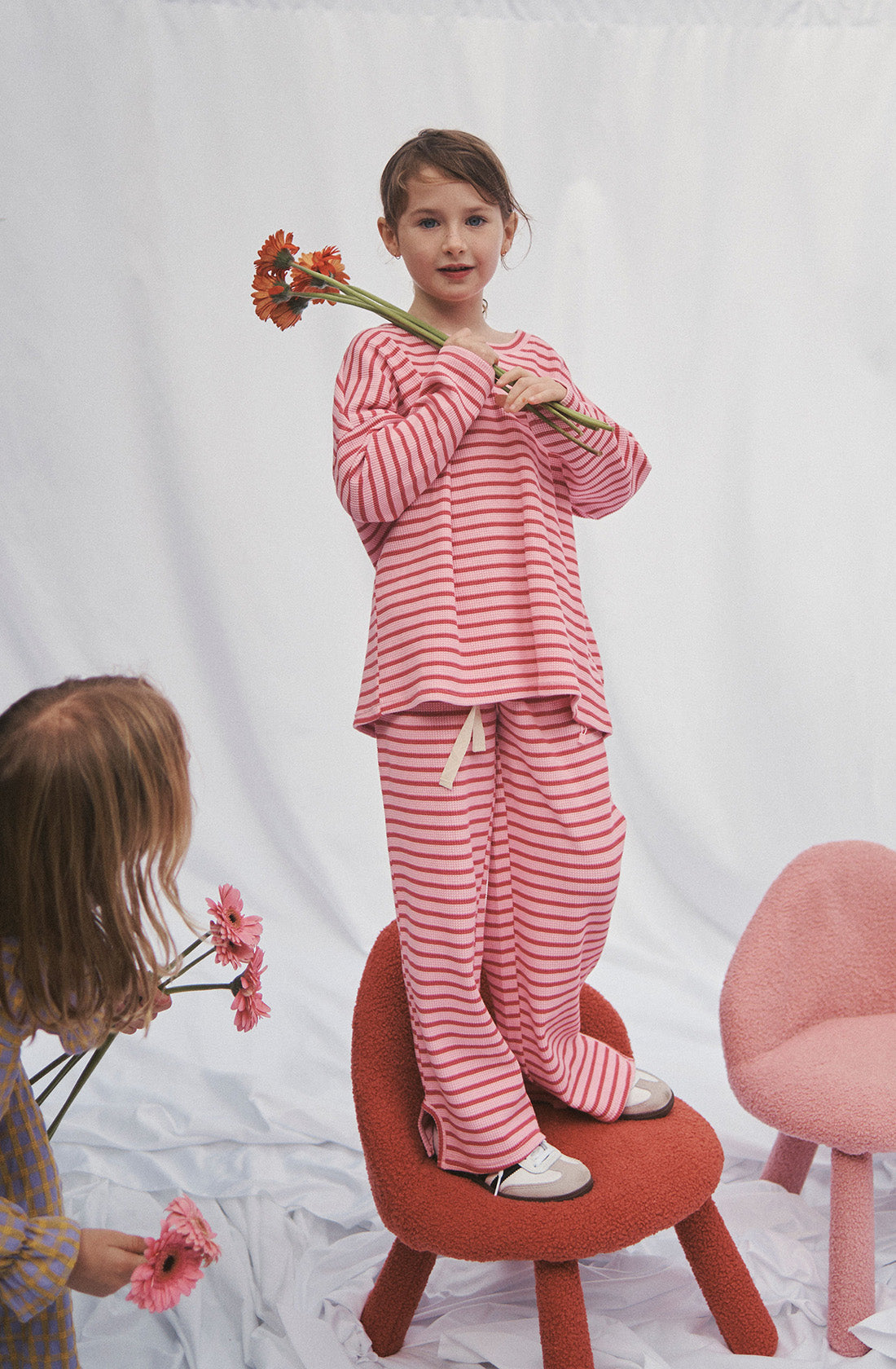 Young kid wearing the lucky lounge pant and matching top in candy apple holding a bunch of flowers while standing on a chair.