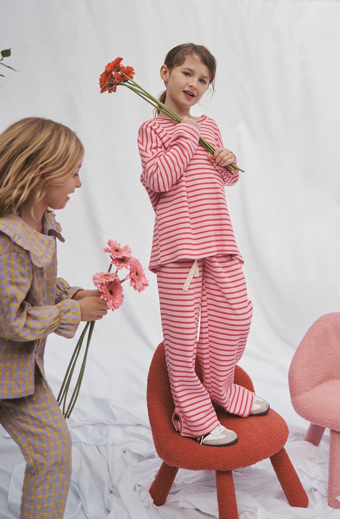 Young kid wearing the lucky lounge pant and matching top in candy apple holding a bunch of flowers while standing on a chair.