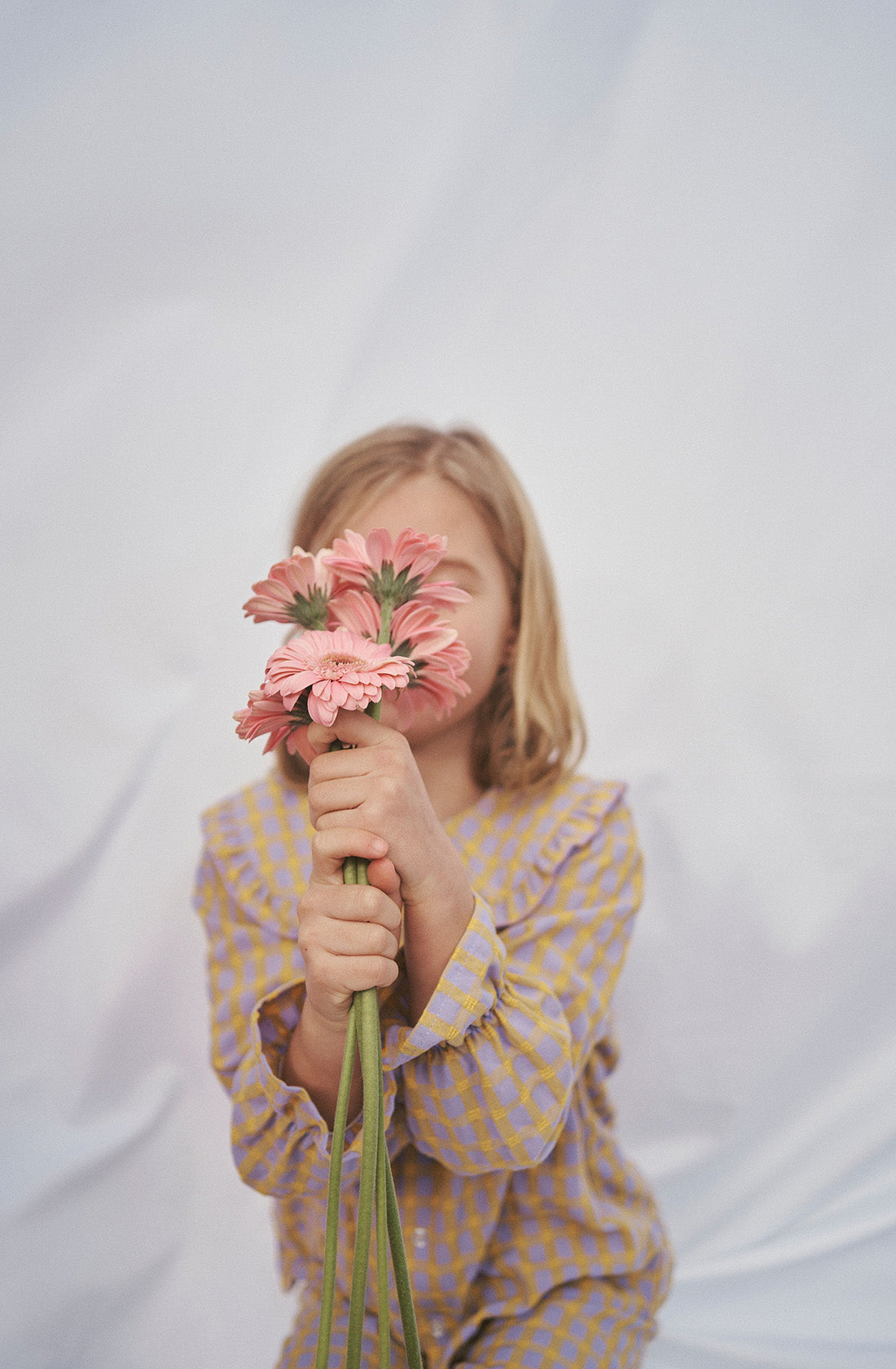 Young kid wearing the Maggie blouse l and matching pant holding a bunch of flowers in front of her face.