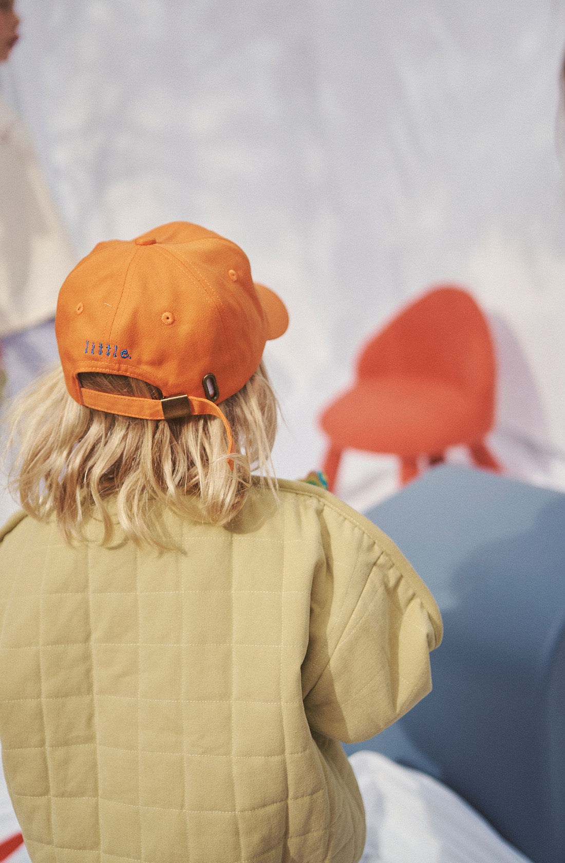 Young kid wearing the parker quilted jacket and an orange cap from behind.