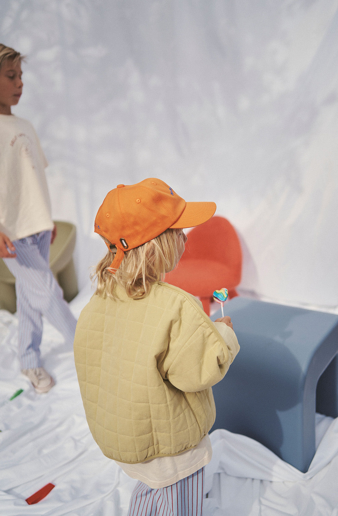 Young kid wearing the parker quilted jacket and orange cap holding a lollypop..