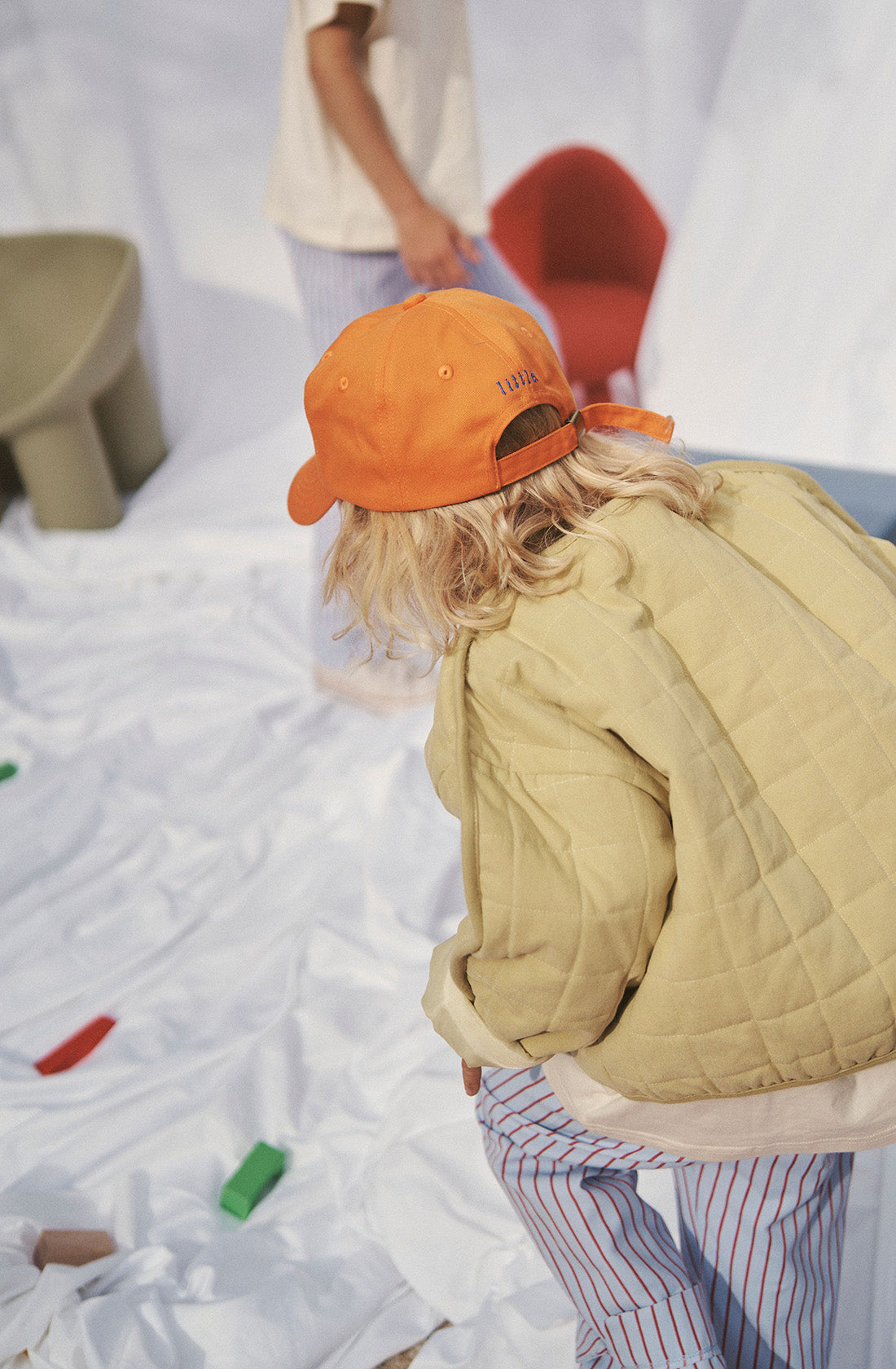 Young kid wearing the parker quilted jacket and striped pants and an orange cap.