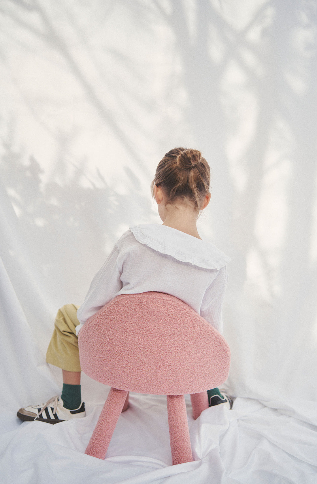 Young kid wearing the Maggie muslin blouse and mustard pants sitting on a chair from the back.