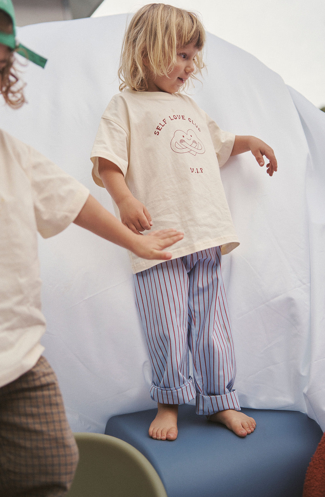 Young kid wearing the party pant blue and red striped in a beige top standing on a chair.