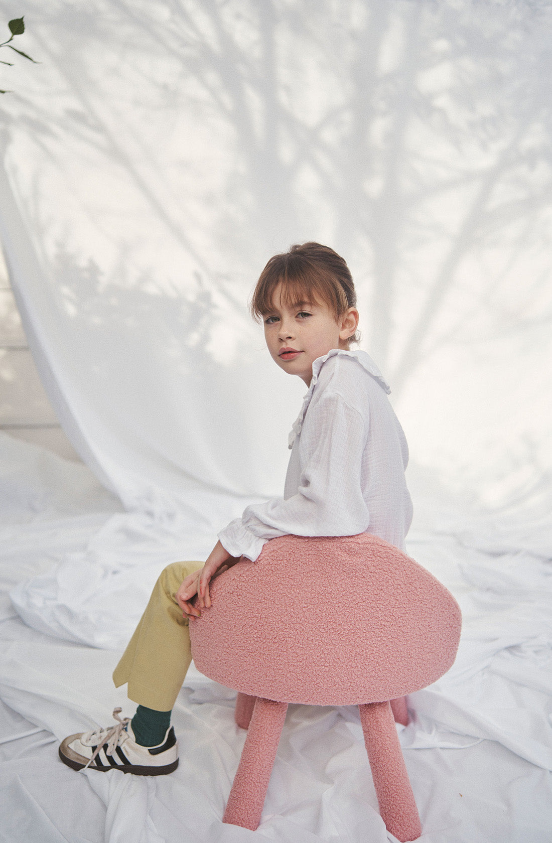 Young kid wearing the Maggie muslin blouse and mustard pants sitting on a chair.