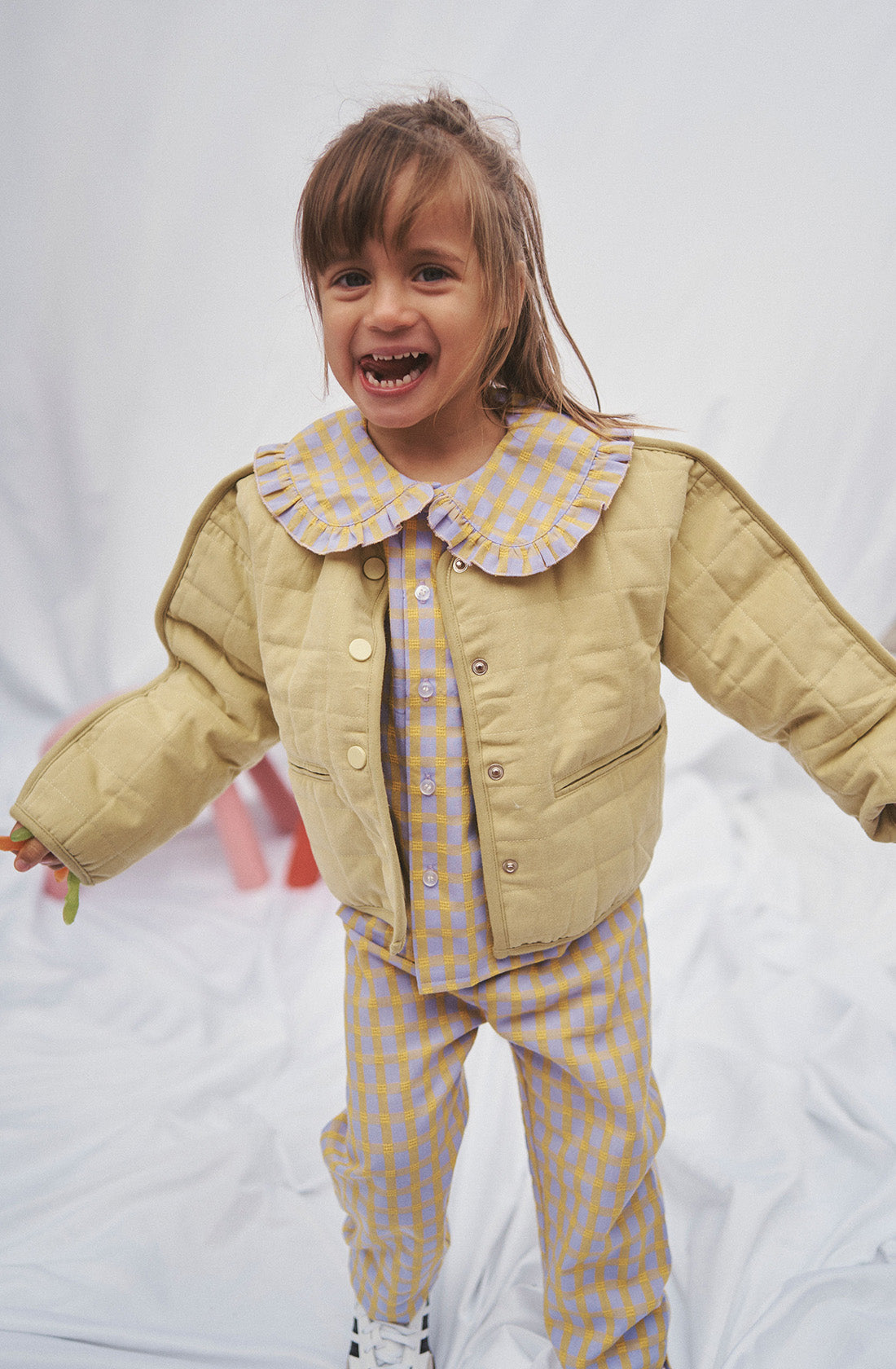 Young kid wearing the Maggie blouse l and matching pant with a yellow jacket over the top.