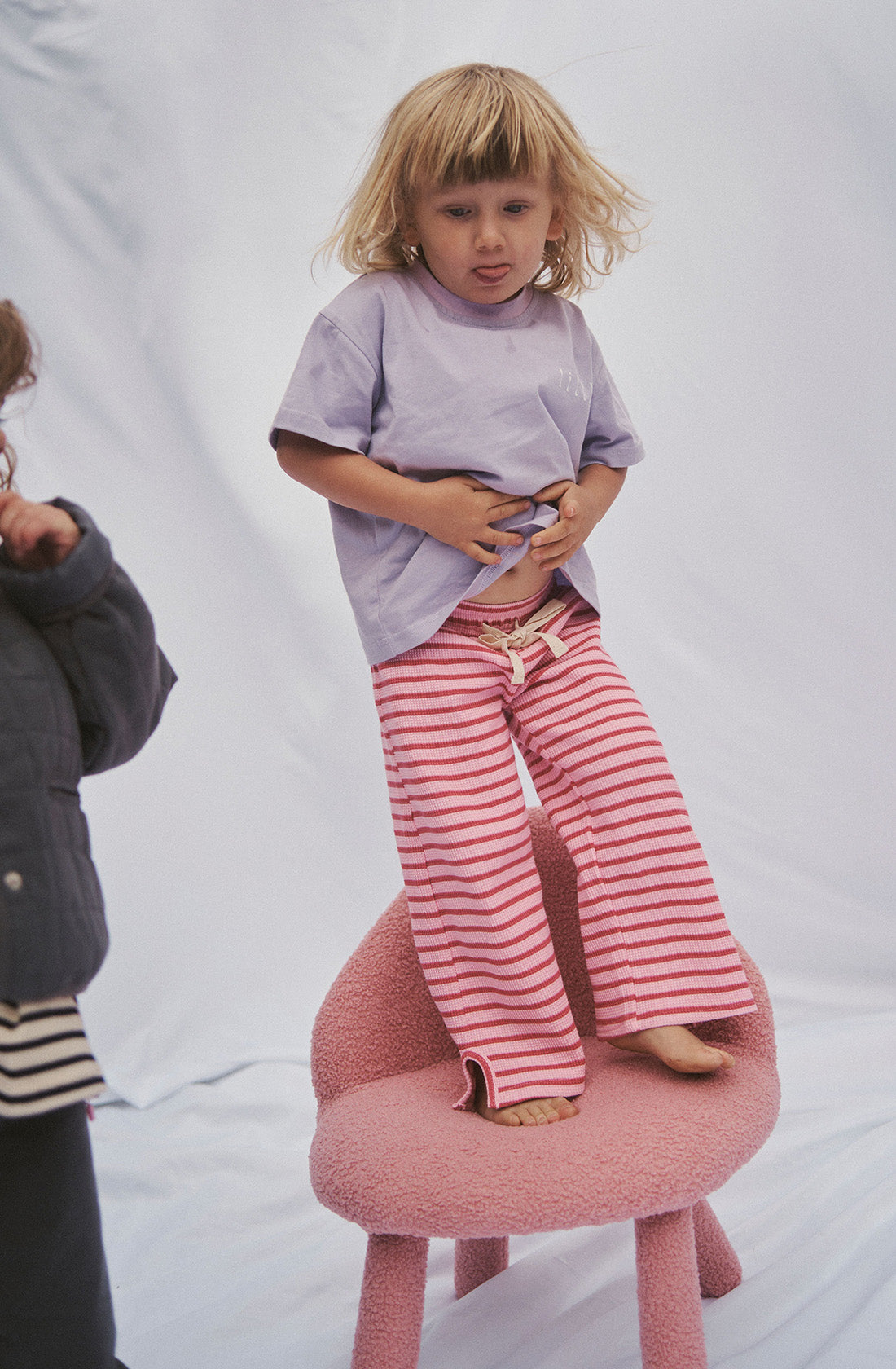 Young kid wearing the lucky lounge pant in candy apple with a purple top standing on a chair..