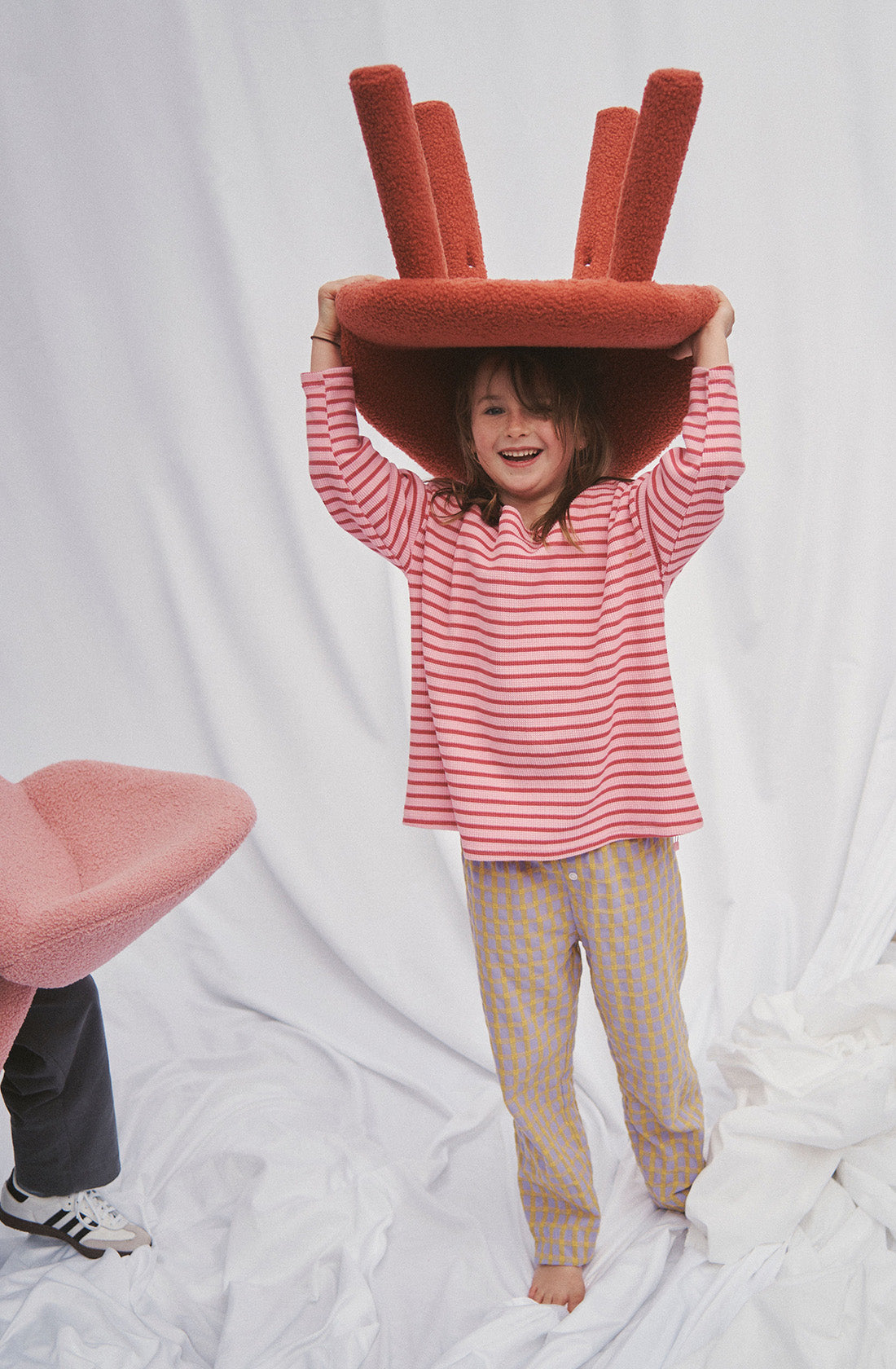 A young girl wearing a red striped long sleeve top holding a chair above her head.