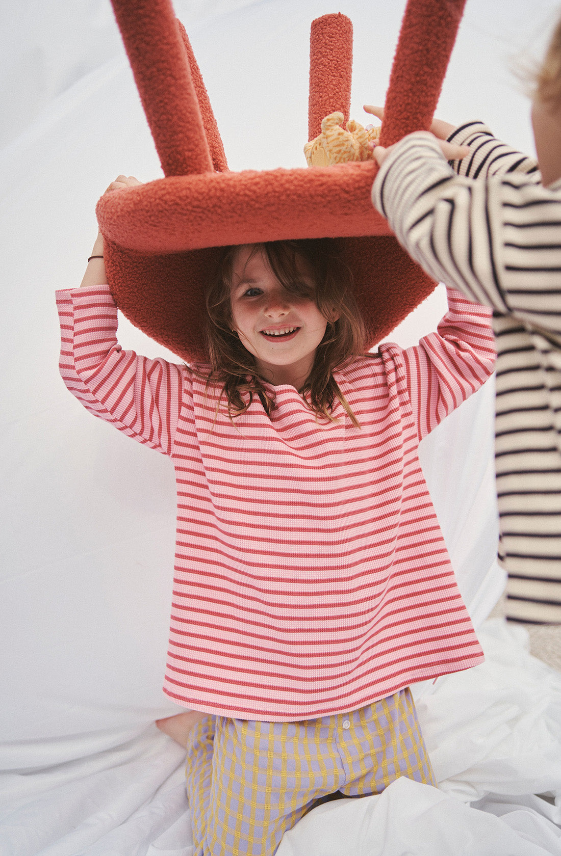 A young girl wearing a striped long sleeve top holding a chair above her head.