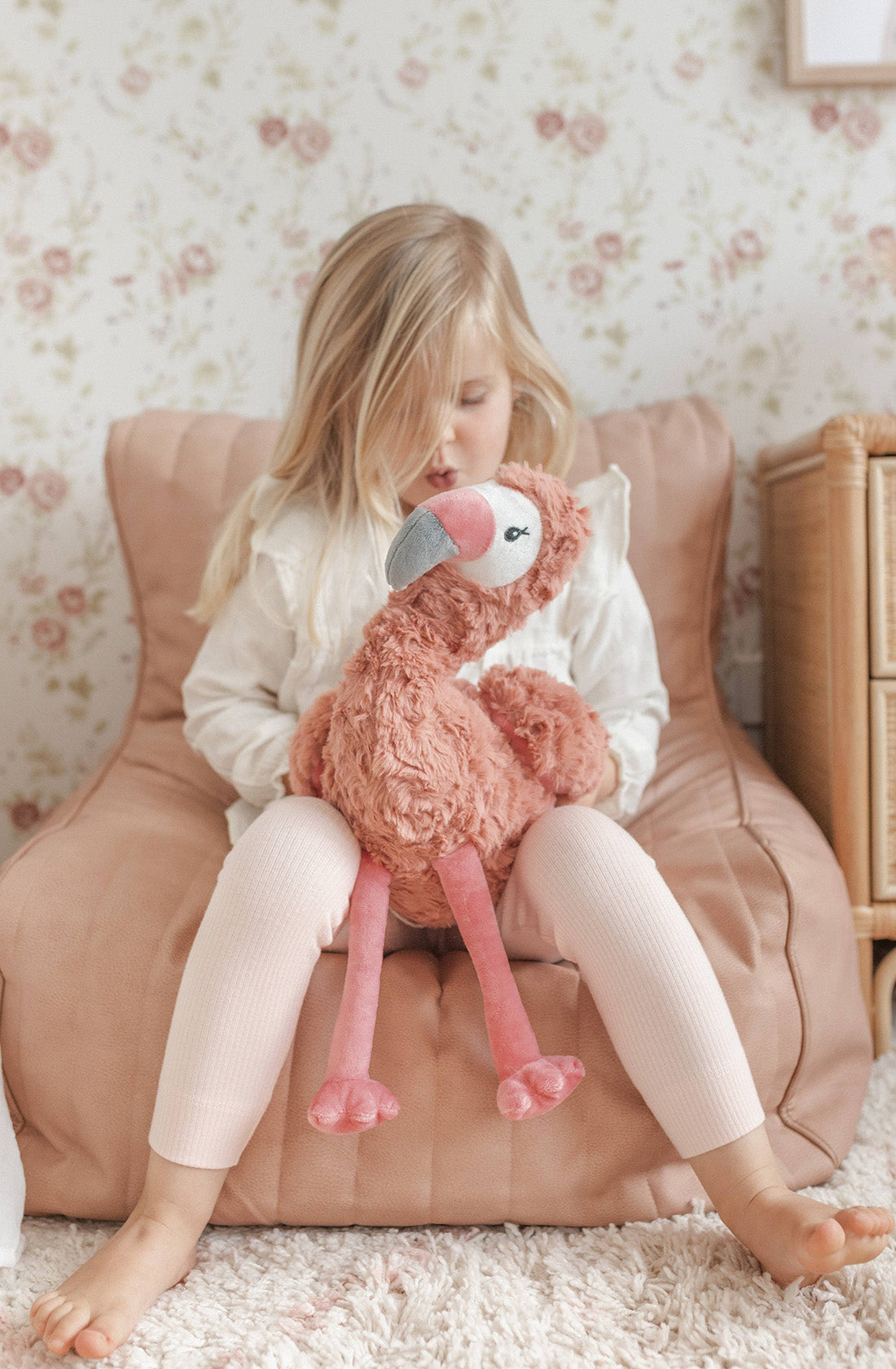 A young kid holding a flamingo weighted toy sitting on a beanbag chair.