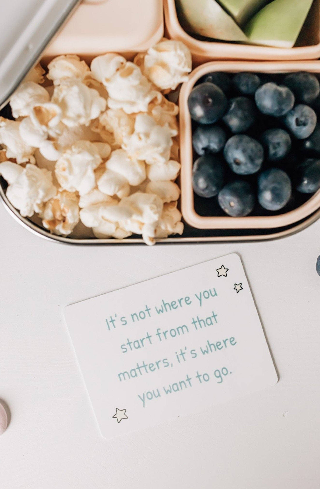 A card on a table next to some popcorn and blue berries saying "it's not where you start that matters, it's where you want to go".